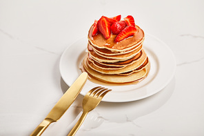 golden fork and knife on plate with pancakes and strawberries