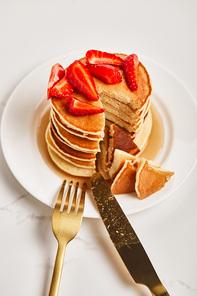 plate with pancakes and slice of pancakes with strawberries near golden cutlery