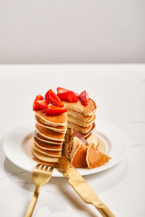 pancakes with strawberries and fork with knife on plate on textured surface
