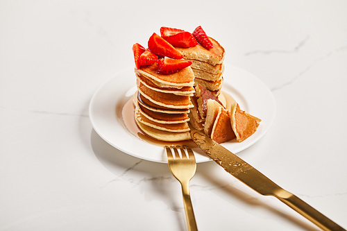 golden cutlery on plate with slice of pancakes with strawberries on textured surface