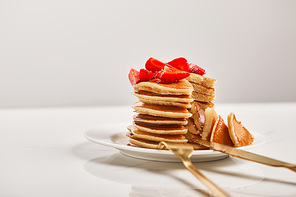 selective focus of pancakes with strawberries and golden cutlery on white plate isolated on grey