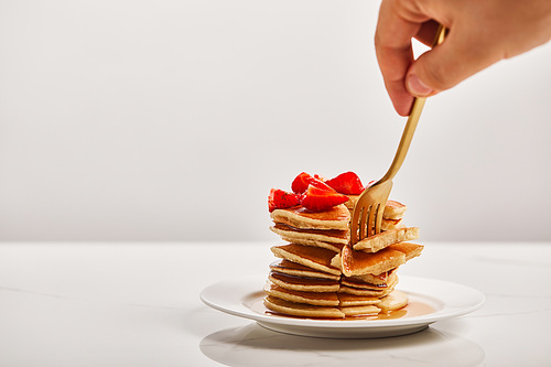 cropped view of man taking slice of pancakes with golden fork on white plate isolated on grey