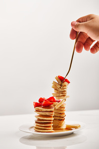 cropped view of man taking slice of pancakes with golden fork from white plate