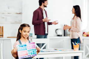 selective focus of cute kid holding paper with colorful stripes while standing near parents at home