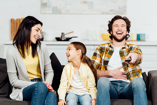 happy father laughing while watching tv near attractive wife and kid