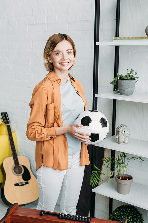 smiling pretty girl in orange shirt and white jeans holding soccer ball
