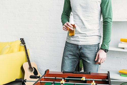 partial view of man standing by football table and holding bottle of beer