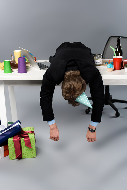 businessman in party cap sleeping on table at messy workplace
