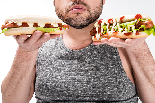 partial view of overweight man holding hot dogs isolated on white