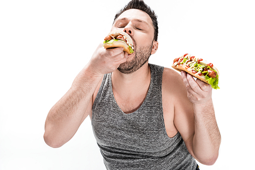 overweight man in tank top eating tasty hot dog isolated on white