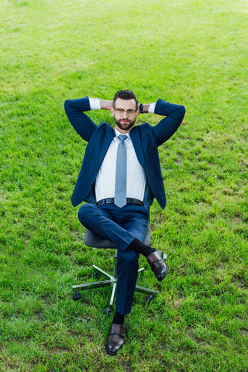 high angle view of businessman sitting in office chair in park with crossed lags and arms behind head