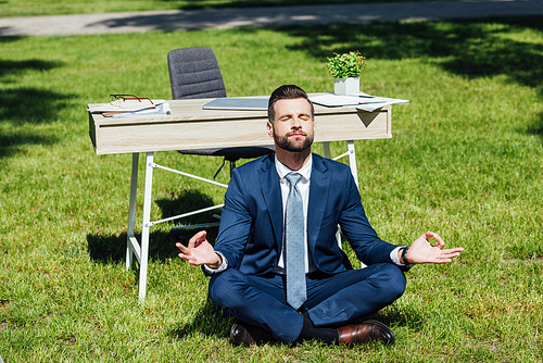 businessman sitting on grass and meditating near table in park