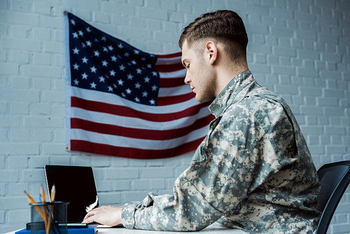 low angle view of handsome soldier using laptop with blank screen