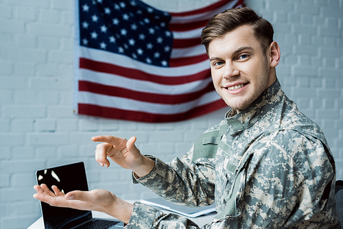 happy military man gesturing in office near laptop with blank screen