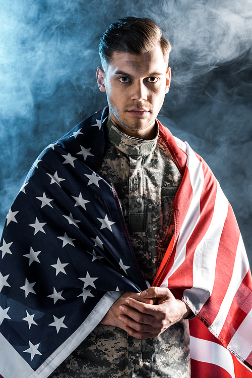 soldier in military uniform with clenched hands and american flag  on black with smoke