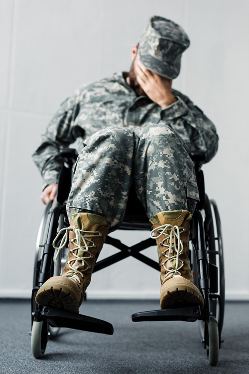 selective focus of disabled military man in uniform sitting in wheelchair and covering face with hand
