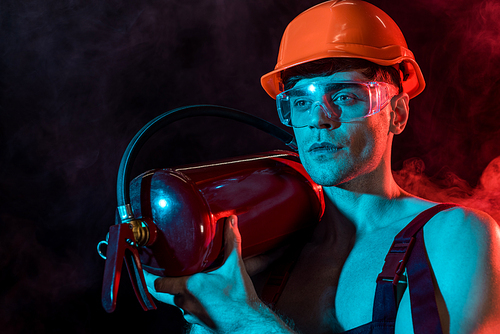 sexy shirtless fireman in overall holding fire extinguisher in smoke on black