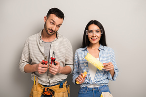 emotional manual workers holding pliers and paint roller on grey