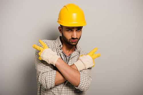 Condescending workman in yellow helmet and gloves gesturing on grey