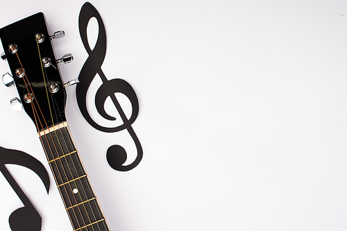 Top view of paper cut music notes and acoustic guitar on white background