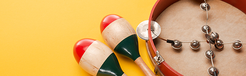 Close up view of tambourine near colorful maracas on yellow background, panoramic shot