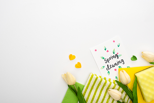 top view of spring tulips, green and yellow cleaning supplies with hearts near spring cleaning card on white background