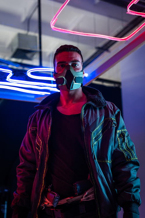 mixed race cyberpunk player in mask standing near neon lighting