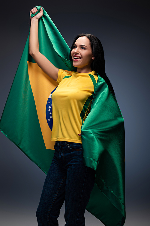 emotional female football fan wrapped in brazilian flag on grey