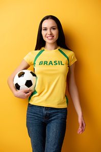 smiling female football fan holding ball on yellow