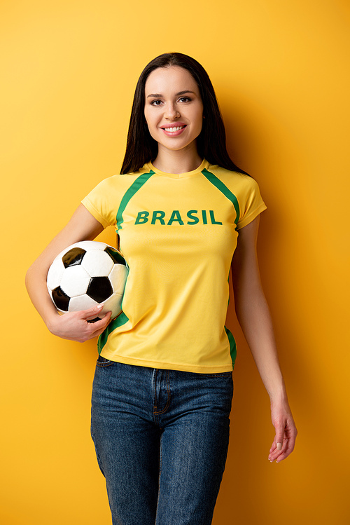 smiling female football fan holding ball on yellow