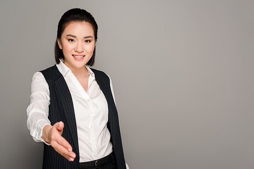 smiling young businesswoman giving hand on grey background