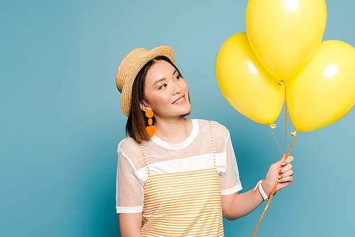 happy asian girl in striped dress and straw hat with yellow balloons on blue background