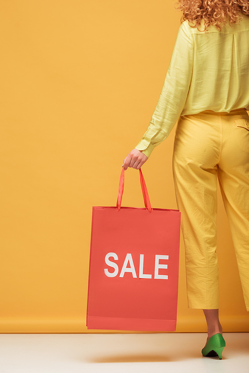 back view of stylish redhead woman holding shopping bag with sale lettering on yellow