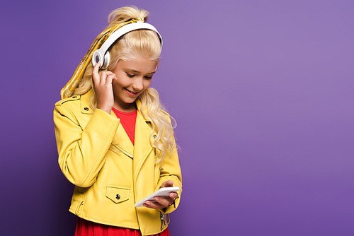 smiling kid with headphones using smartphone on purple background