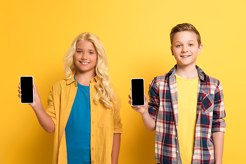 smiling kids holding smartphones with copy space on yellow background