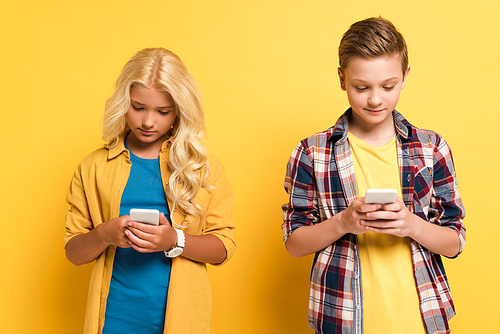 smiling and cute kids using smartphones on yellow background