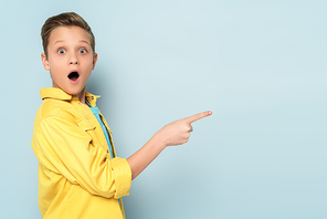 shocked and cute kid pointing with finger on blue background