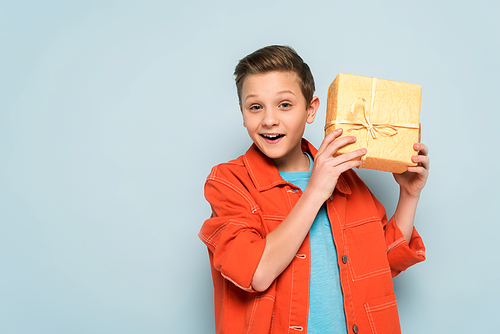 smiling and cute kid holding gift box on blue background