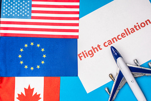 Top view of flags of canada, european union and america near toy plane with flight cancellation lettering on card on blue surface