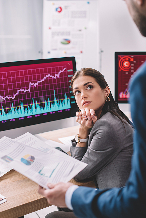 Selective focus of data analyst looking at colleague holding papers with graphs in office