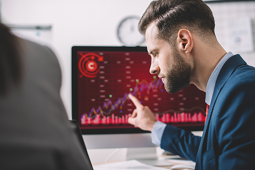 Selective focus of analyst pointing on charts on computer monitor while working with colleague in office