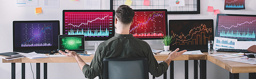 Back view of data analysts sitting at table with computers and charts in office, panoramic shot