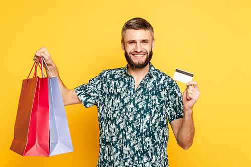 happy bearded guy with shopping bags and credit card on yellow