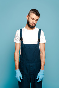 sad cleaner in uniform and rubber gloves on blue background