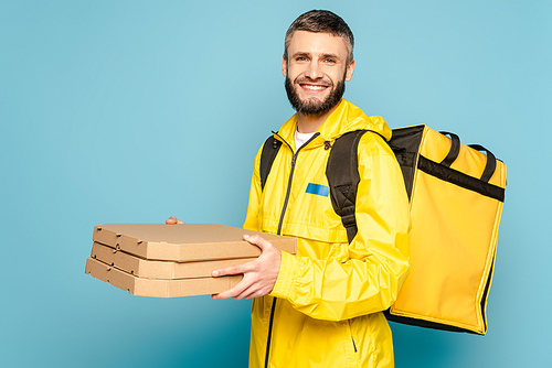 smiling deliveryman in yellow uniform with backpack holding pizza boxes on blue background