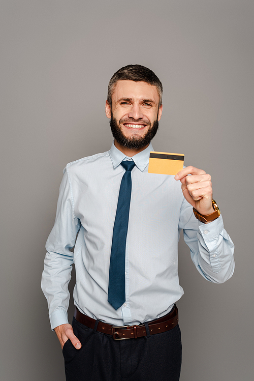 smiling handsome bearded businessman with credit card on grey background