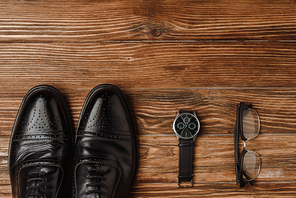 Flat lay with mens black shoes, wristwatch and glasses on wooden background