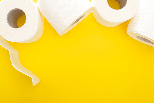 top view of white toilet paper rolls on yellow background with copy space