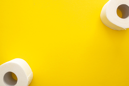 top view of clean toilet paper rolls on yellow background with copy space