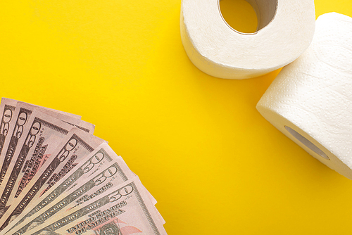 top view of white toilet paper rolls and dollars on yellow background